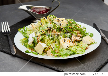 Fresh green salad with chicken, brie cheese, and sesame seeds, served with berry sauce on the side 117421149