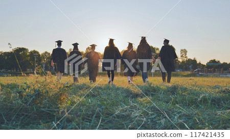 Graduate students walking through an evening meadow at sunset. 117421435