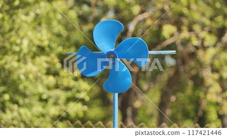 A blue vane weathervane spins in the wind in the summer. A blue vane weathervane spins in the wind in the summer. 117421446