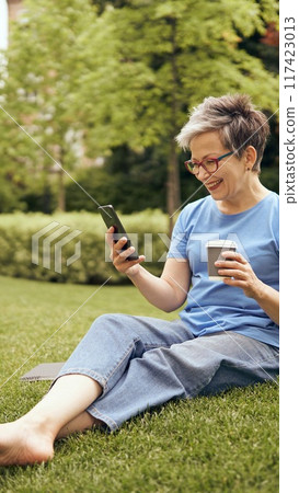 Savoring coffee and enjoying technology while relaxing in a peaceful park setting 117423013