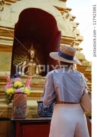 A woman wearing a straw hat stands in front of a gold and red building 117423861
