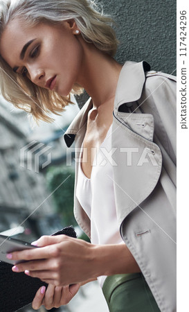 An Urban Fashion Influencer Poses with a Smartphone While Dressed in a Trendy Outfit 117424296