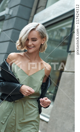 A Stylish Woman in a Green Dress and Jacket Gracefully Strolling Along City Streets A Stylish Woman in a Green Dress and Jacket Gracefully Strolling Along City Streets 117424312