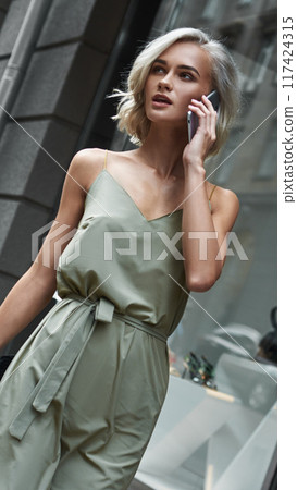 A Chic Woman is found in a Modern Cityscape, Engaged in a Conversation on Her Phone 117424315