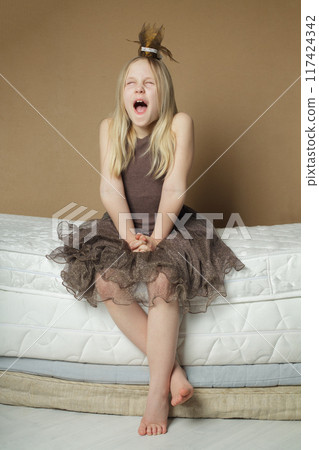 Young blonde girl yawning and sitting on mattress at home Young blonde girl yawning and sitting on mattress at home 117424342