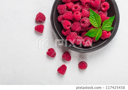 fresh raspberries, on a black plate, with leaves, top view, on a white table, 117425438