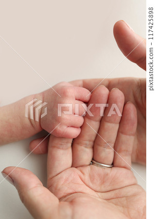 The newborn baby has a firm grip on the parent's finger after birth. Close-up little hand of child and palm of mother and father. Parenting, childcare and healthcare concept. The newborn baby has a firm grip on the parent's finger after birth. Close-up little hand of child and palm of mother and father. Parenting, childcare and healthcare concept. 117425898