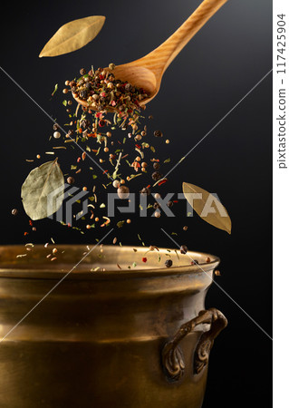 Mix of dried spices is poured into a old brass pan. 117425904