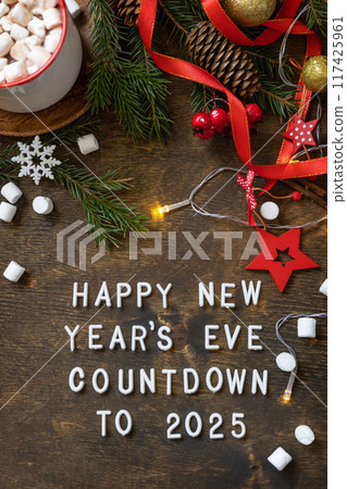Winter, christmas lights, cozy cup hot chocolate drink with marshmallow on wooden table background. View from above with english text Happy New Year's Eve countdown to 2025. Winter, christmas lights, cozy cup hot chocolate drink with marshmallow on wooden table background. View from above with english text Happy New Year's Eve countdown to 2025. 117425961