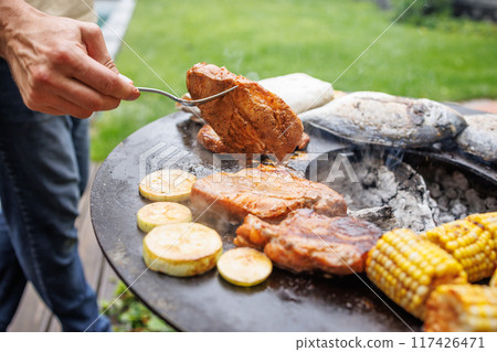 Outdoor barbecue with grilled fish, meat steaks and vegetables, man cooking on grill in garden Outdoor barbecue with grilled fish, meat steaks and vegetables, man cooking on grill in garden 117426471