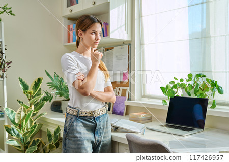 Portrait serious thoughtful teenage girl looking out the window, at home Portrait serious thoughtful teenage girl looking out the window, at home 117426957