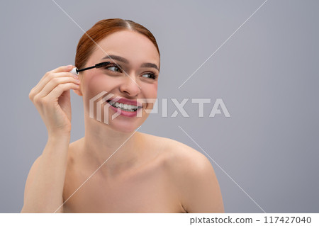 Young woman applying mascara to long eyelashes 117427040