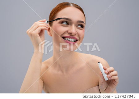 Young female model applying black mascara to lashes 117427043