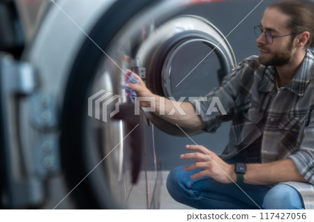 Hard working bearded man washing clothes at self-service laundromat 117427056
