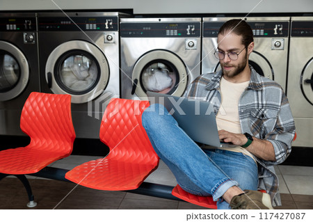 Man using wireless internet and laptop while waiting for washer at laundromat 117427087