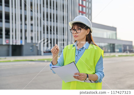 Industrial worker female builder with working documents, outdoor construction 117427323