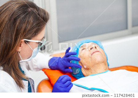 Dermatologist carrying out a skin biopsy on the face of a senior adult patient 117428401