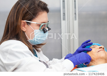 Dermatologist carrying out a skin biopsy on the face of a senior adult patient 117428406