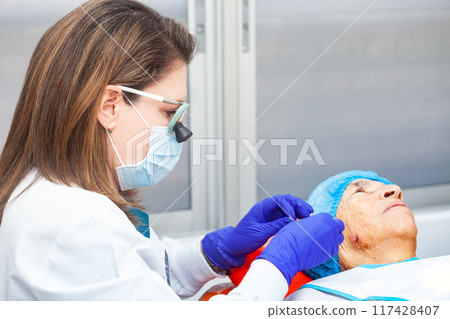 Dermatologist carrying out a skin biopsy on the face of a senior adult patient 117428407