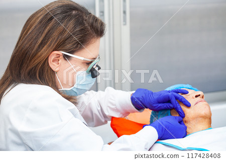 Dermatologist carrying out a skin biopsy on the face of a senior adult patient 117428408