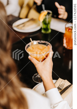 Enjoying a refreshing cocktail during a cozy gathering with friends at a stylish restaurant 117428591