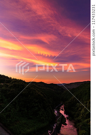 Summer 2024 Evening view of Nunome Dam in eastern Nara City. The sky is burning on the north (valley) side of the dam. Bands of crimson clouds and the crimson-colored Nunome River. 117433231