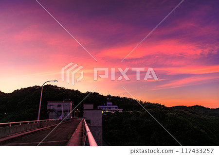 Summer 2024 Evening view of Nunome Dam in eastern Nara City. The sky is burning on the north (valley) side of the dam. A blanket of crimson clouds spreads out to the north of the dam. 117433257