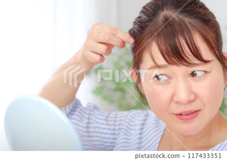 A woman in her 40s checking her hair A woman in her 40s checking her hair 117433351