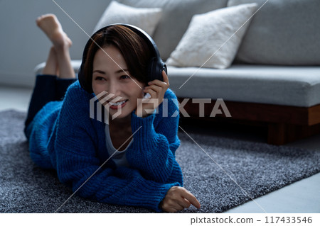 Middle-aged woman lying on carpet listening to music 117433546