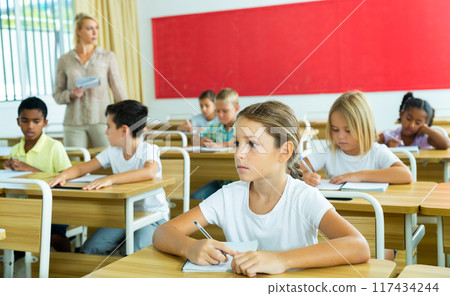 Diligent tween girl studying with classmates in elementary school Diligent tween girl studying with classmates in elementary school 117434244
