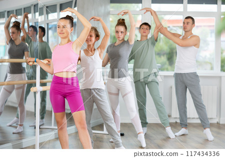 Teacher conducts class with teen girls and boys in ballet studio, observes doing Batman exercise. Teacher conducts class with teen girls and boys in ballet studio, observes doing Batman exercise. 117434336