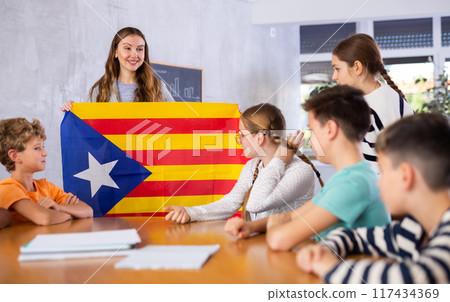 Young female teacher holding colorful flag of Estelada while working with preteens in classroom 117434369