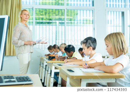 Diligent tweens studying in classroom with female teacher 117434393