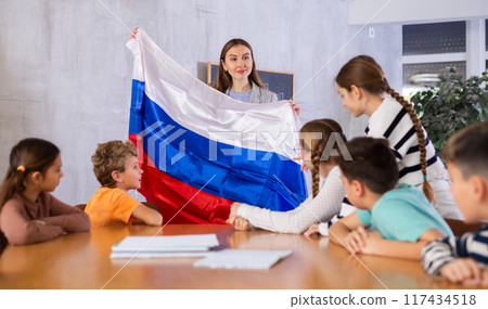 Pupils having lesson of geography. Female teacher discussing with children about national flag of Russia 117434518