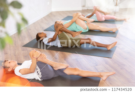 Girls and boys doing abdominal crunches with outstretched arms to strengthen abs and core muscles during group yoga class in studio 117434520