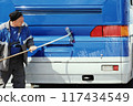 Uniform-clad individual thoroughly washes the back side of a bus, focusing on the taillights area 117434549