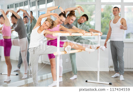 Teen ballet students prepare for classes, near ballet bare stretch legs under man teacher guidance 117434559