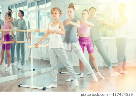Teacher conducts class with teen girls and boys in ballet studio, observes doing Batman exercise. 117434589
