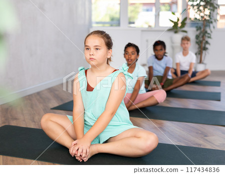 Group of children practicing yoga in lotus pose, meditating together in studio 117434836
