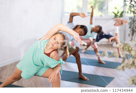 Children standing in Parivrtta Trikonasana or Revolved Triangle Pose on mats during group yoga training in fitness center Children standing in Parivrtta Trikonasana or Revolved Triangle Pose on mats during group yoga training in fitness center 117434944
