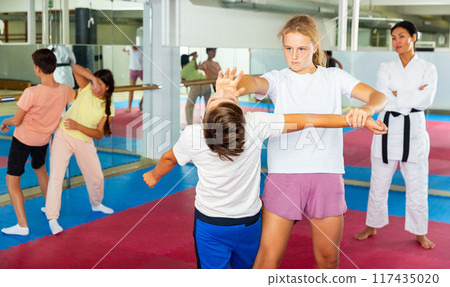 Kids in pair exercising self-defense movements during group class with female coach 117435020