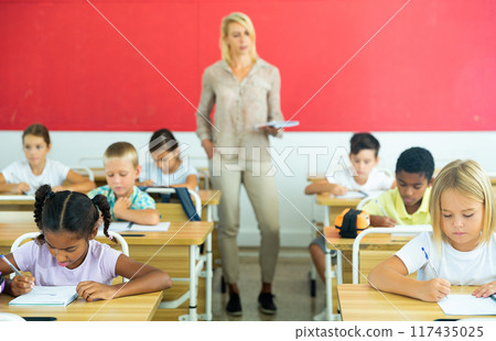 Diligent tweens studying in classroom with female teacher 117435025