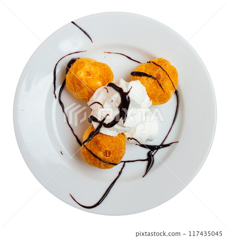 Exquisite profiteroles. Traditional French choux pastry balls filled with sweet custard garnished with vanilla cream Exquisite profiteroles. Traditional French choux pastry balls filled with sweet custard garnished with vanilla cream 117435045