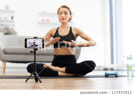 Woman filming online yoga class at home with smartphone 117437011