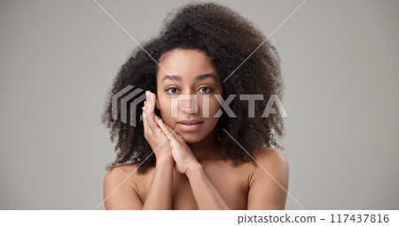 Beauty and Healthcare concept - Beautiful African American woman with curly afro hairstyle hair and clean, healthy skin on gray studio background posing and looking at camera Beauty and Healthcare concept - Beautiful African American woman with curly afro hairstyle hair and clean, healthy skin on gray studio background posing and looking at camera 117437816