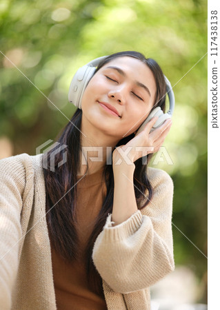 A woman wearing headphones is smiling and appears to be enjoying her music A woman wearing headphones is smiling and appears to be enjoying her music 117438138