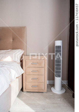 Modern bedroom with sleek tower fan and beige nightstand. Modern bedroom with sleek tower fan and beige nightstand. 117438437