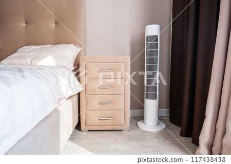 Modern bedroom with sleek tower fan and beige nightstand. Modern bedroom with sleek tower fan and beige nightstand. 117438438