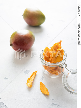 Dried mango slices with two fresh raw mangoes. 117438956