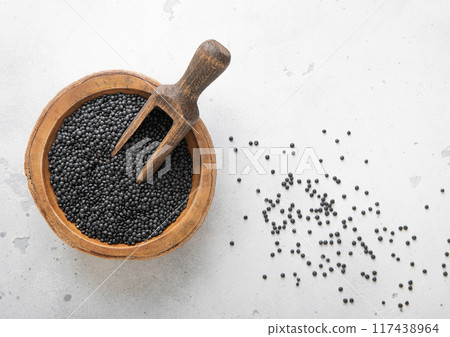 Raw dry black lentils seeds in wooden bowl with scoop on light table. Raw dry black lentils seeds in wooden bowl with scoop on light table. 117438964